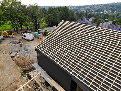 Układanie pierwszej warstwy izolacji na zewnętrznej ścianie wentylowanej na budowie w Bielsku-Bałej, widok na dach